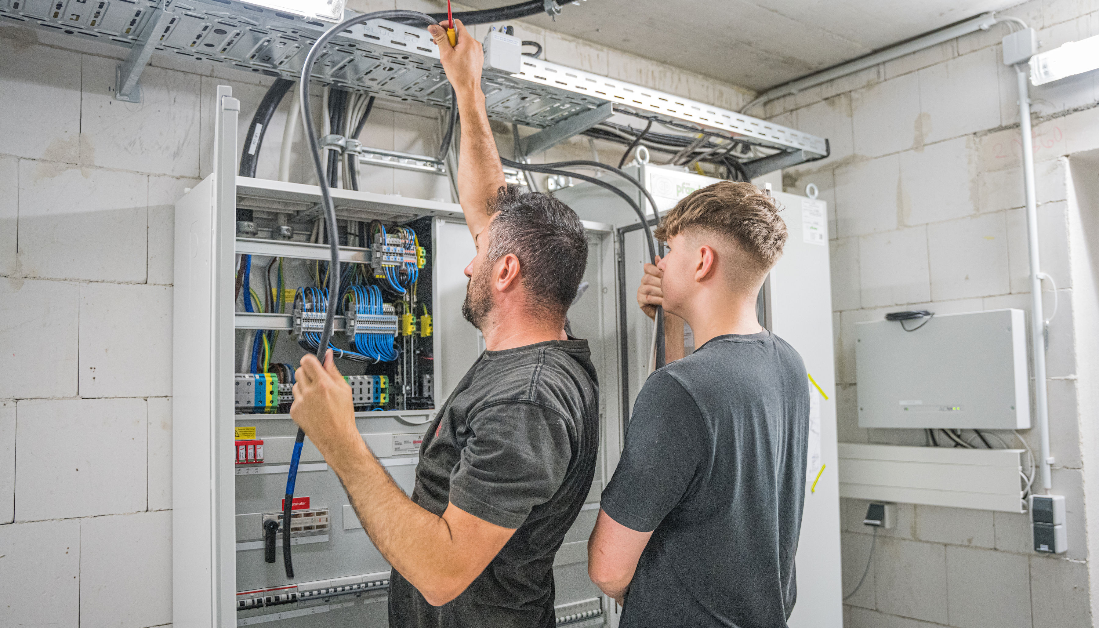 Zwei Männer arbeiten an einem Netzwerkkabel in einem Sicherungskasten.