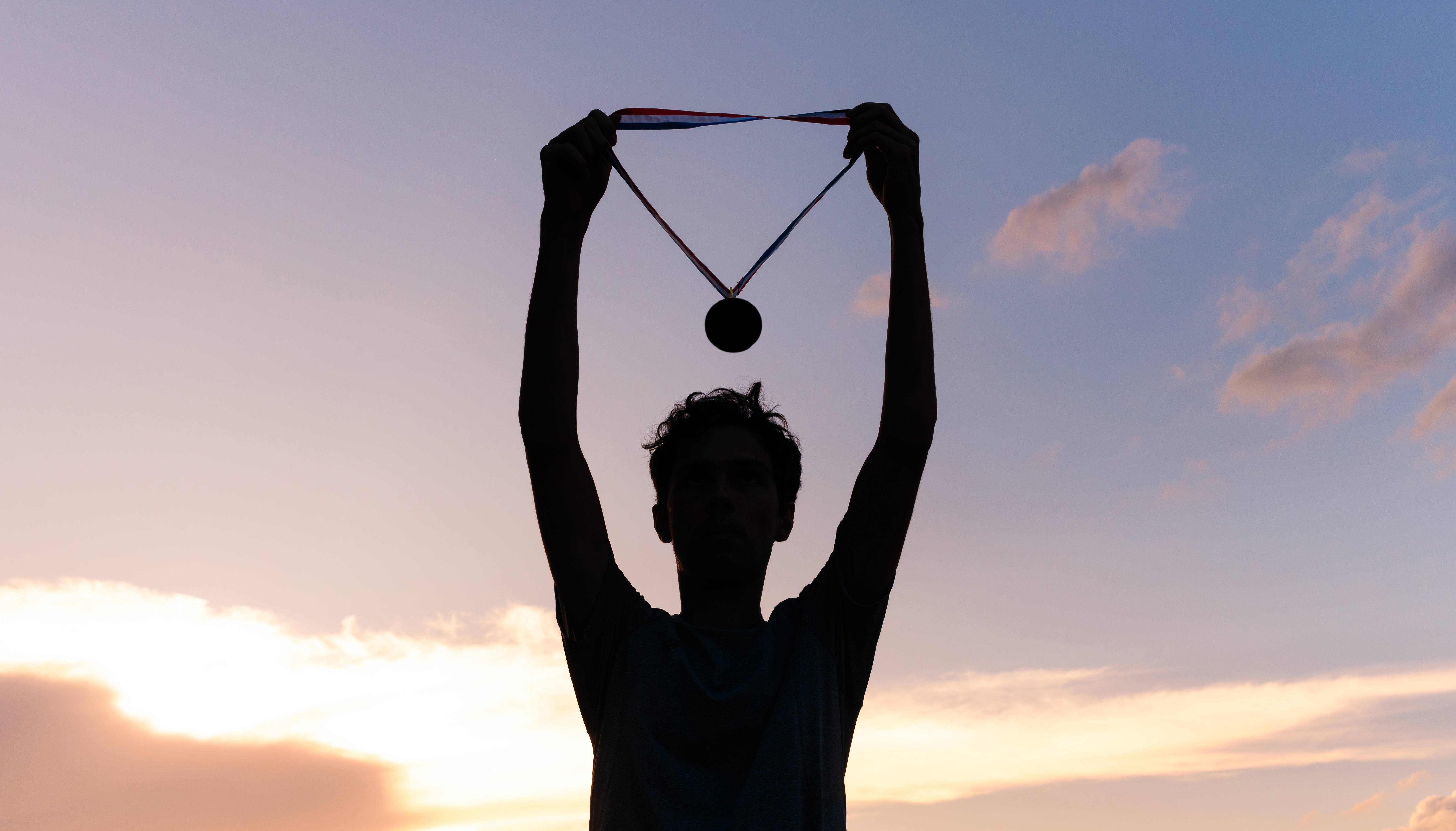 Junger Mann hält Medaille in der Abendsonne hoch