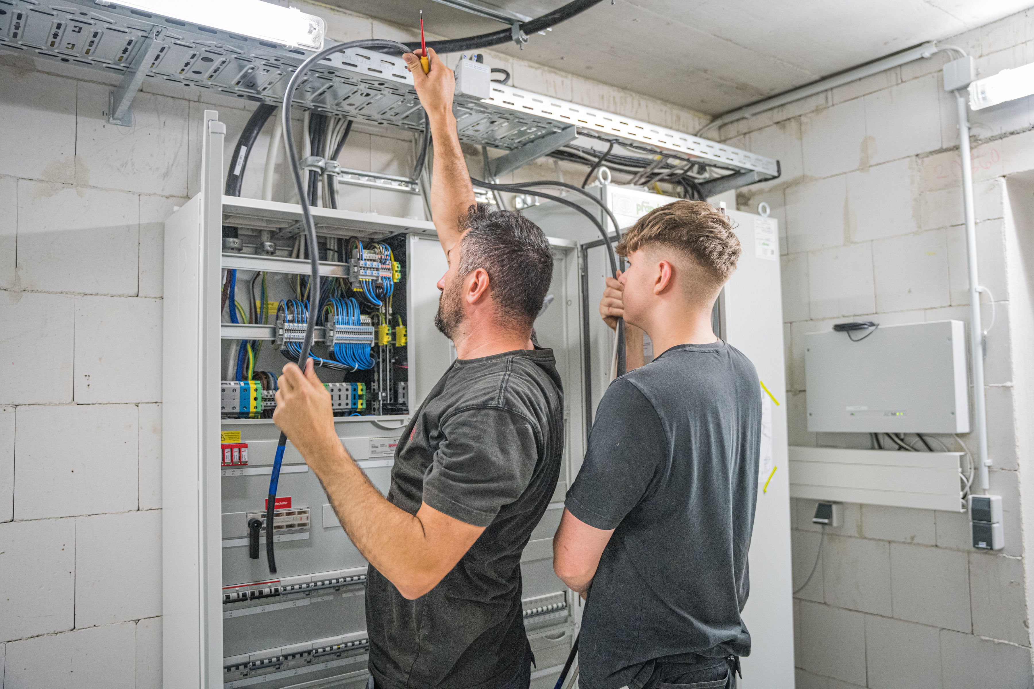 Zwei Männer arbeiten an einem Netzwerkkabel in einem Sicherungskasten.