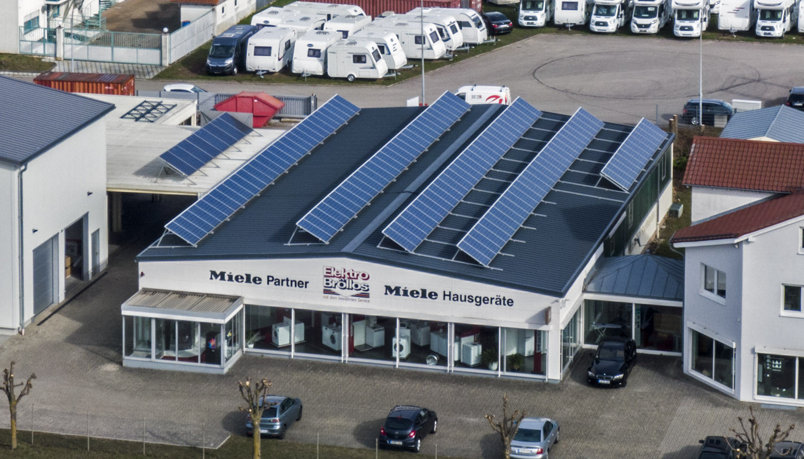Firmebgebäude des Miele Partners Elektro BRÖLLOS mit Solaranlagen auf Dach und Showroom mit Waschmaschinen.