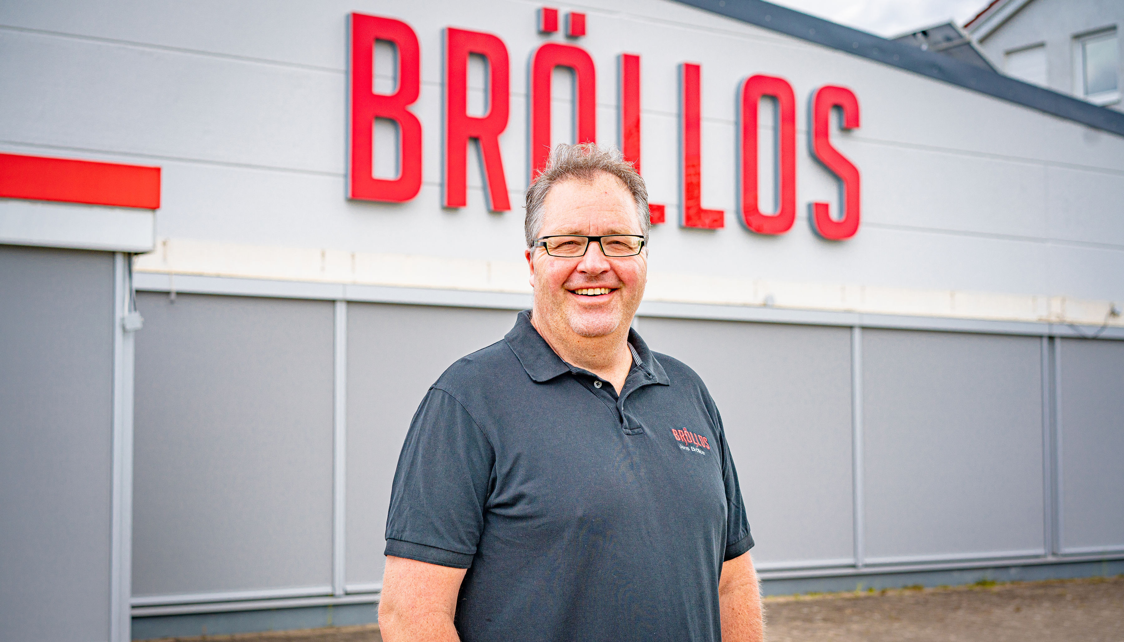 Jens Bröllos vor dem Firmengebäude mit Logo
