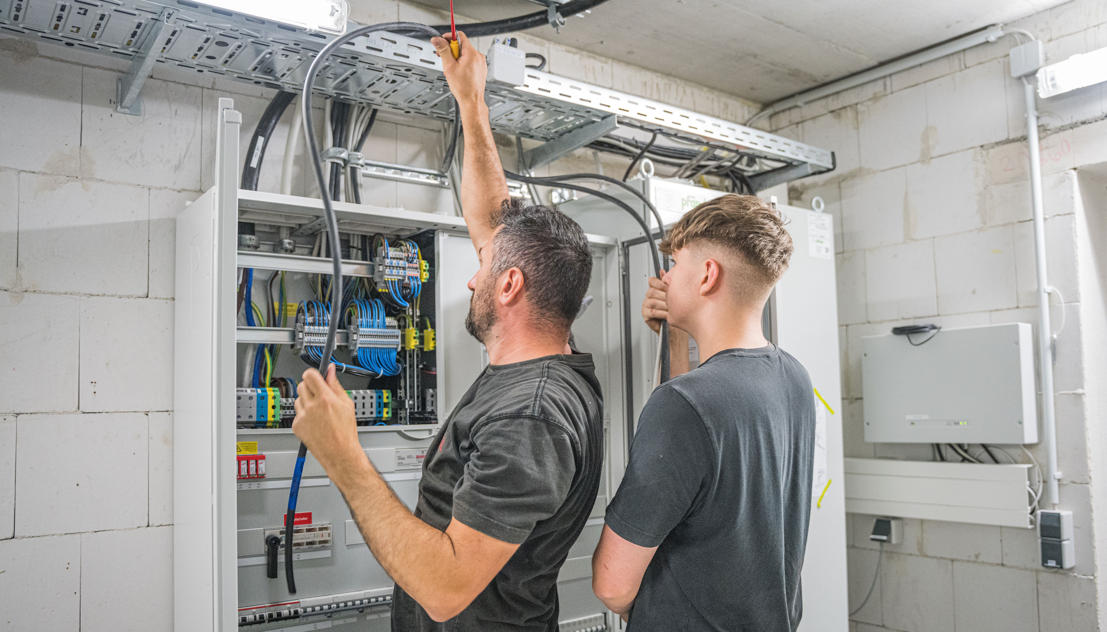 Zwei Männer arbeiten an einem Netzwerkkabel in einem Sicherungskasten.