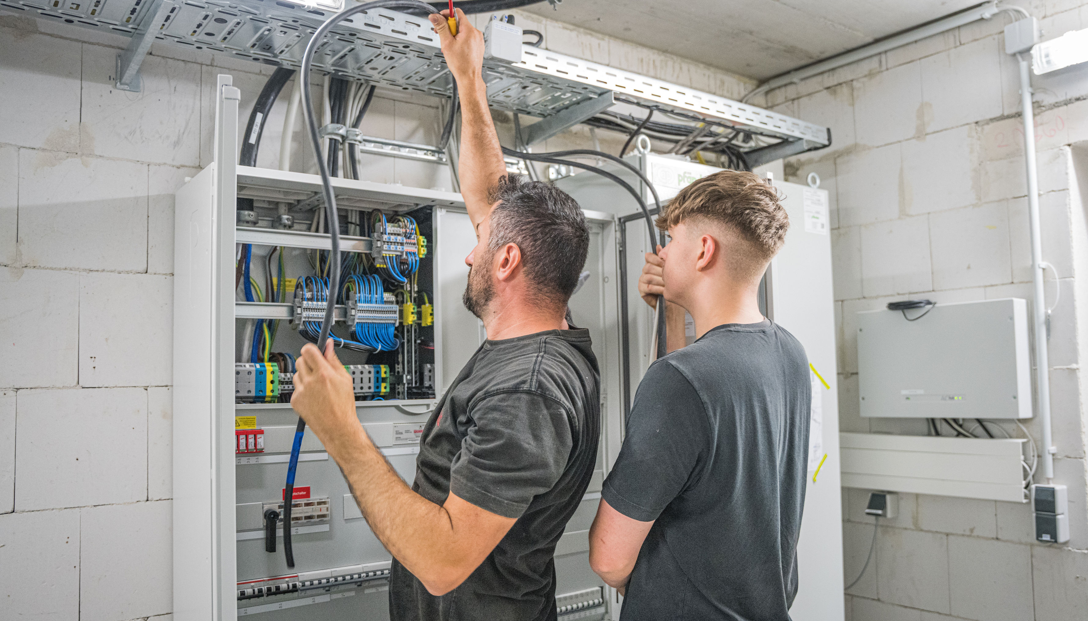 Zwei Männer arbeiten an einem Netzwerkkabel in einem Sicherungskasten.